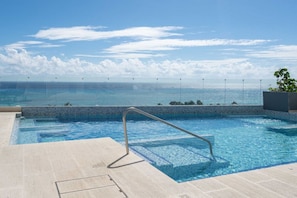 Piscina com vista para o oceano, uma escada de metal e um deck revestido com azulejos.