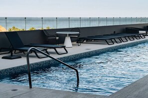 A poolside area with lounge chairs, a table, and a view of the ocean.