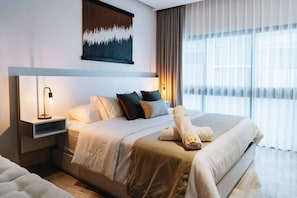 A modern hotel room with a large bed, a bedside table with a lamp, a painting on the wall, and a window with curtains.