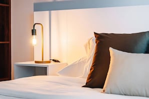 Une chambre d’hôtel avec un lit, des oreillers, une table de chevet et une lampe.