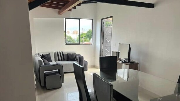Una sala de estar moderna con una mesa de comedor de vidrio, un sofá gris y un televisor sobre un mueble de madera.