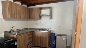 Cocina pequeña con gabinetes de madera, pileta integrada, estufa a gas, refrigerador Samsung y un refrigerador compacto.