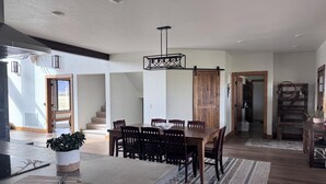 A spacious kitchen with a large island, wooden dining table, and chairs. There is a staircase leading to another level, and a wooden door. - The Rendezvous - Mountain views surrounded by fields (Cody)