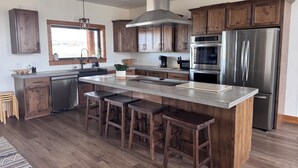 A modern kitchen with wooden cabinets, stainless steel appliances, and a central island with stools. - The Rendezvous - Mountain views surrounded by fields (Cody)