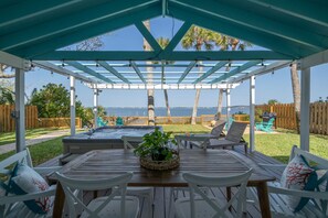 A covered patio with a wooden table and chairs, a hot tub, and a view of the ocean.