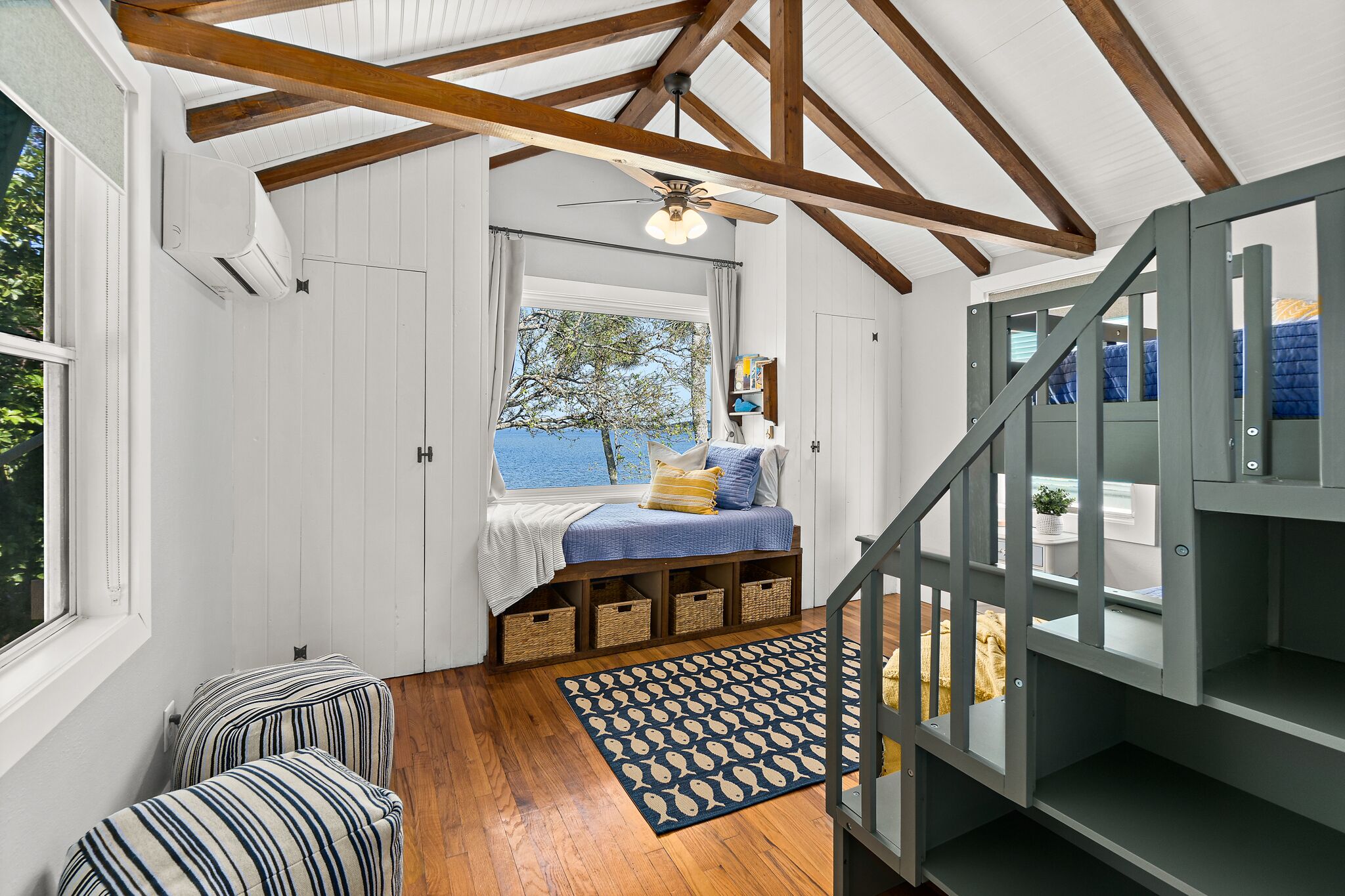 A cozy room with a wooden ceiling, a bed with a view, a staircase, and a window.