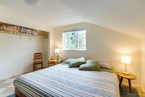 Quarto com cama, cadeira, mesa de cabeceira com luminária, janela e ventilador de teto.