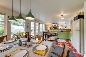 Uma área de refeições com uma mesa posta para quatro pessoas, uma cozinha ao fundo e vista para o exterior através de grandes janelas.