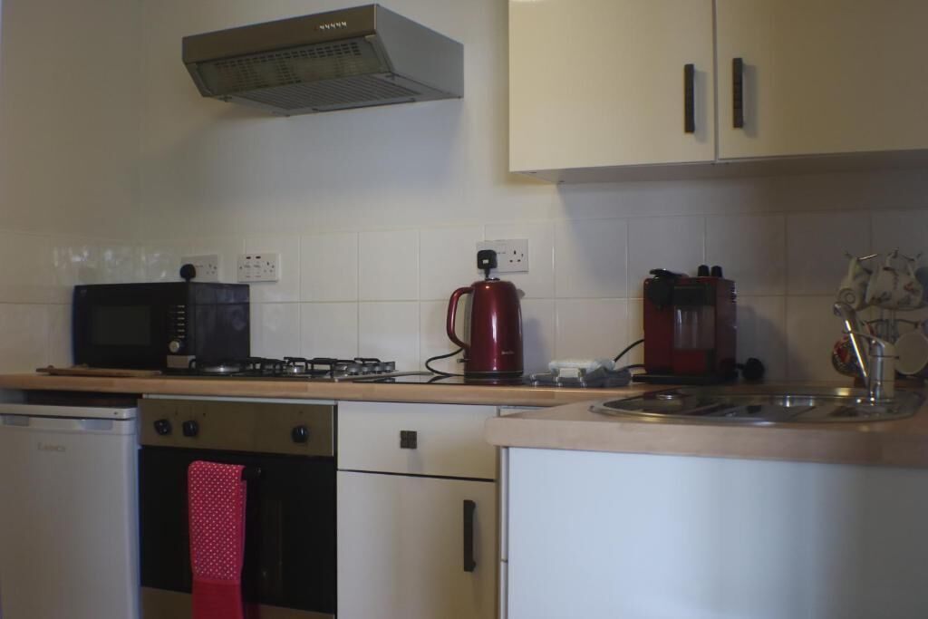 A kitchen with a microwave, stove, red kettle, and a sink.