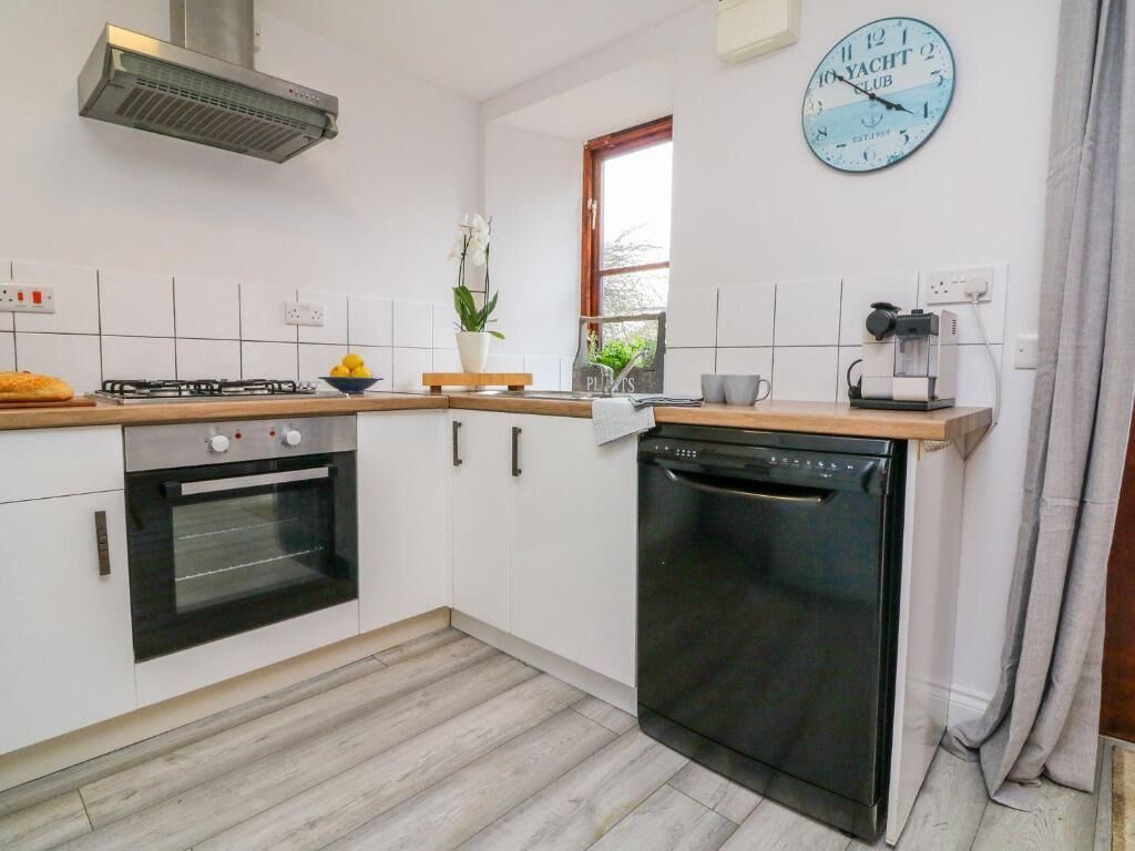 A kitchen with white cabinets, a black oven, a dishwasher, a clock, and a window with a view.