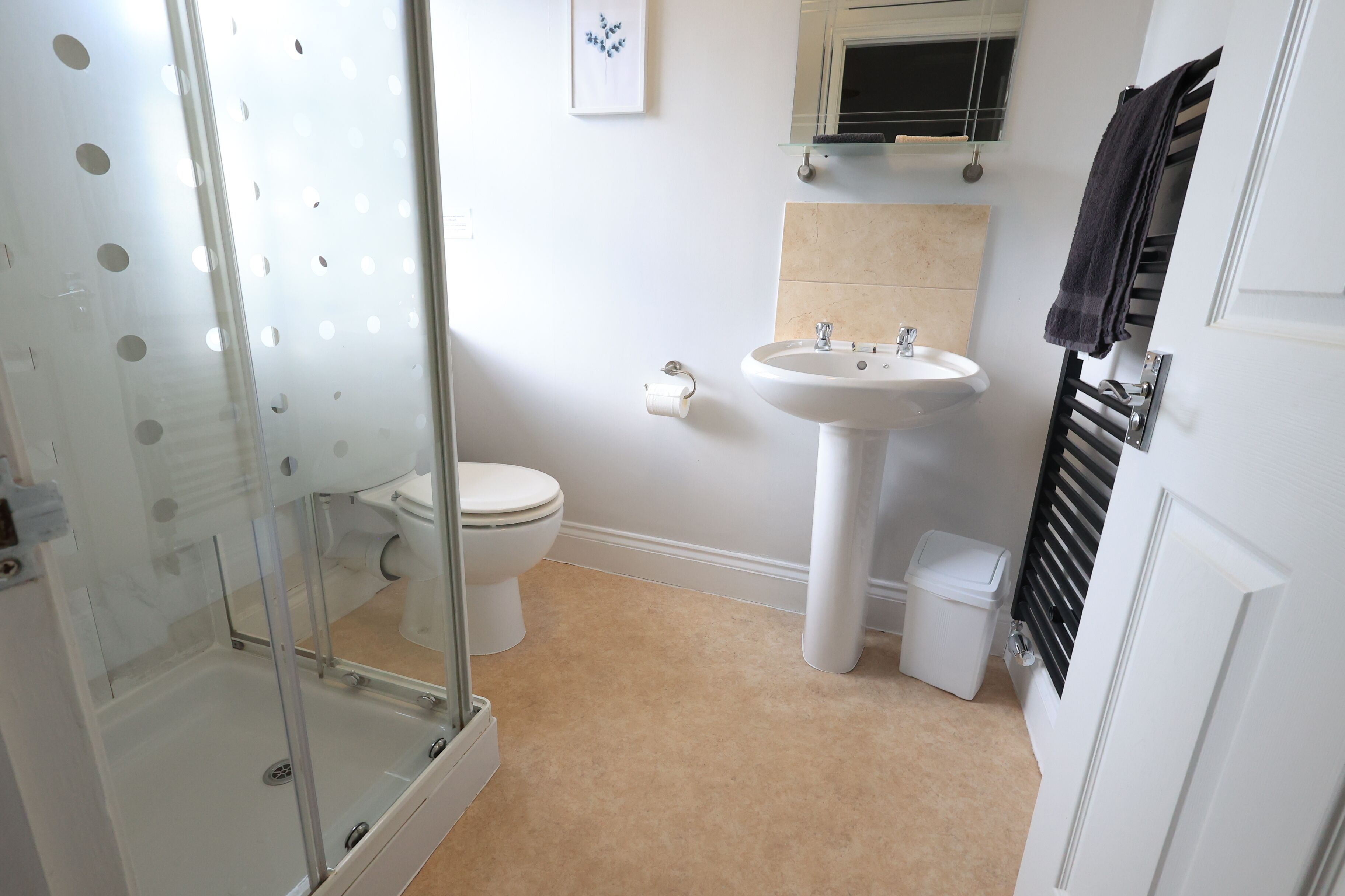 A bathroom with a glass shower enclosure, a white toilet, a sink, and a towel rack.