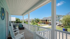 A covered porch with white railings, a set of white rocking chairs, and a view of neighboring houses. - The Teal Turtle: Beautiful, spacious home with easy beach access (Oak Island)