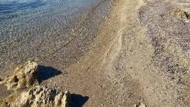 A clear beach with pebbles and a rocky shoreline.
