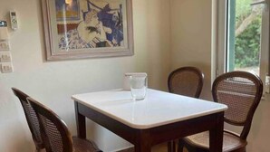 A dining area with a square table and four wicker chairs. A framed artwork is on the wall above the table.