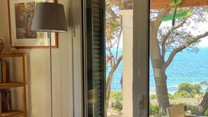 A room with wicker chairs, a bookshelf, and a view of the sea.