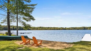 A lakeside setting with two Adirondack chairs, a green canoe, and a white dock extending into the water. - Two Homes: 1-Hot Tub; 2-Lakefront w/Dock, Big Yard (Pullman)