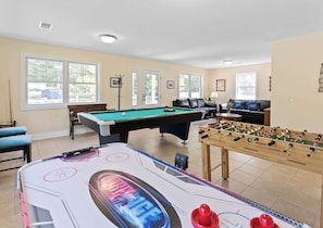 A pool table, foosball table, and seating area in a well-lit room with large windows.