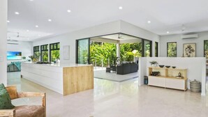 A spacious, modern living area with a central island, large windows, and a view of greenery. - House Heliconia | Luxury Palm Cove Retreat with Private Pool & Lush Gardens (Palm Cove)