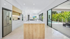 A modern kitchen with a central island, stainless steel appliances, and a view of a swimming pool. - House Heliconia | Luxury Palm Cove Retreat with Private Pool & Lush Gardens (Palm Cove)