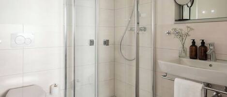 A modern bathroom with a glass-enclosed shower, a white toilet, a sink with a mirror, and a small wooden stool.
