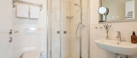 A modern bathroom with a glass-enclosed shower, a white toilet, a sink with a mirror, and a towel rack.