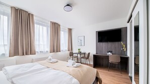 Habitación de hotel con cama, escritorio, silla, televisor y ventana con cortinas.