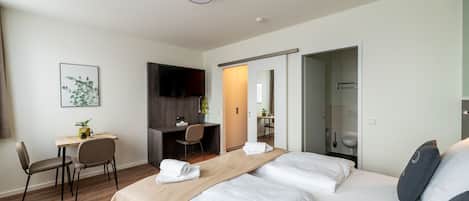 A modern hotel room with a large bed, a desk, and a shower area.