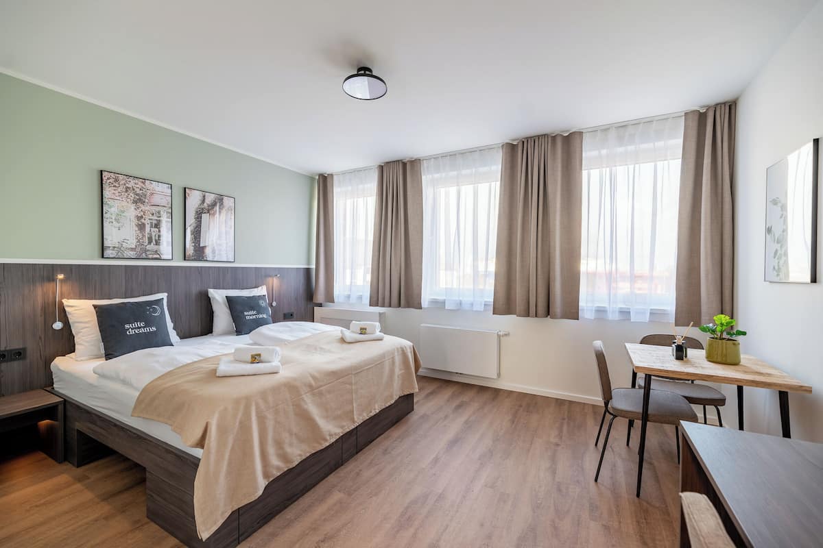 Ein Hotelzimmer mit Bett, Nachttischen, Schreibtisch, Stuhl und einem Fenster mit Vorhängen.