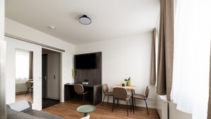 Una sala de estar moderna con un sofá gris, una pequeña mesa redonda y un comedor con una mesa y sillas de madera.