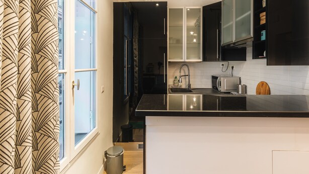 A modern kitchen with a black countertop, white cabinets, and a window with patterned curtains.