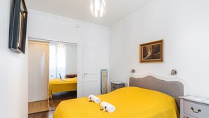 A hotel room with a bed, a nightstand, a mirror, a painting, and a door leading to another room.