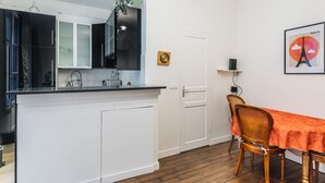 A compact kitchen with white cabinets, a black countertop, and a wooden dining table with an orange tablecloth.