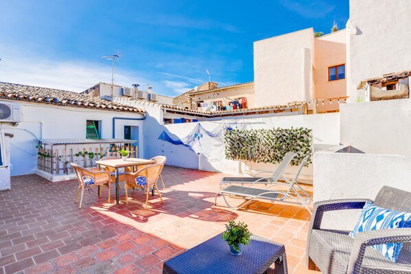 A rooftop patio with a table and chairs, a lounge chair, and a small table with a plant.