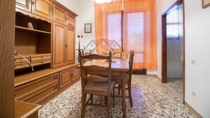 Un coin repas avec une table et des chaises en bois, une cuisine avec des placards en bois et une fenêtre agrémentée de rideaux orange.