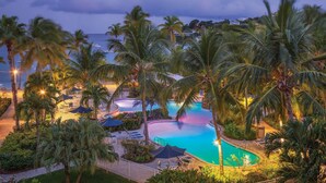 A resort pool area with palm trees, lounge chairs, and a view of the sea. - Beautiful Secluded Island Getaway (St. Thomas)