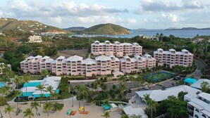 A resort with multiple hotel buildings, a beach area with palm trees, and a view of the sea and hills in the background. - Beautiful Secluded Island Getaway (St. Thomas)