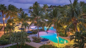 A resort pool area with palm trees, lounge chairs, and a view of the sea. - Beautiful Secluded Island Getaway (St. Thomas)