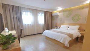 Una habitación de hotel con una cama grande, un escritorio con planta, un televisor y un ventanal con cortinas.