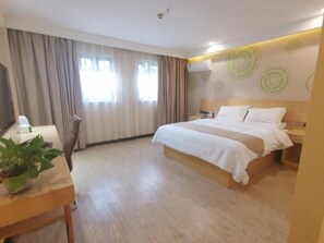Una habitación de hotel con una cama grande, un escritorio con planta, un televisor y un ventanal con cortinas.