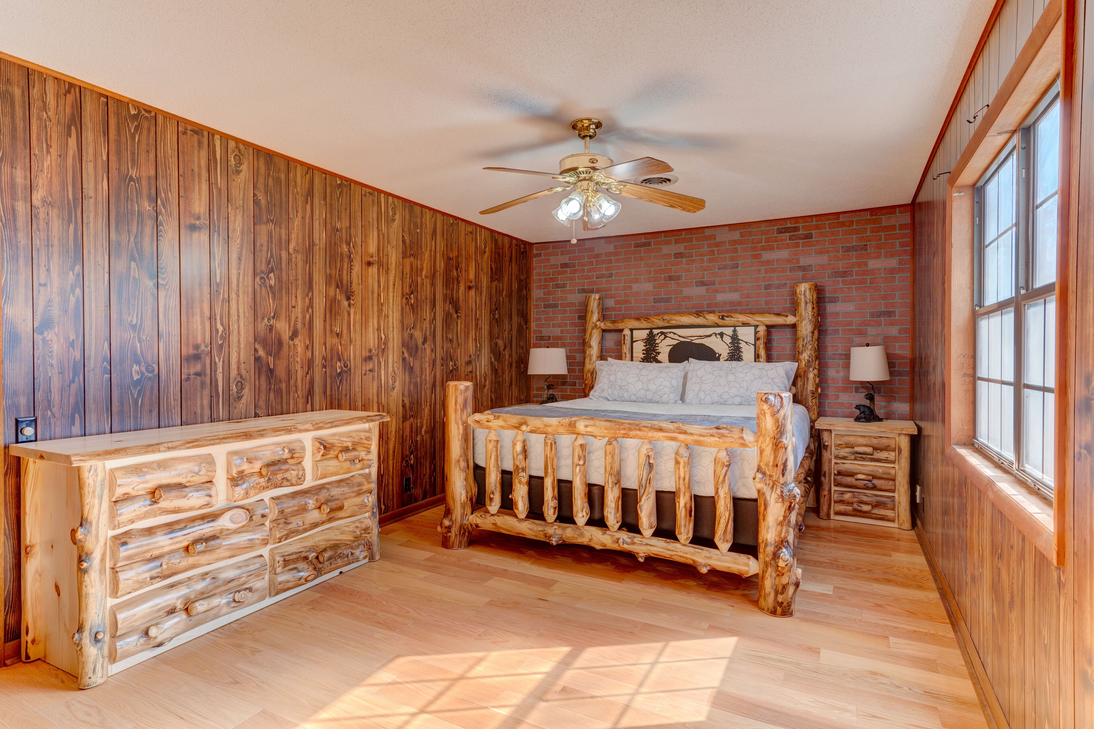 Une chambre à coucher rustique avec un lit en bois, une commode en bois, un ventilateur de plafond et un mur en briques.