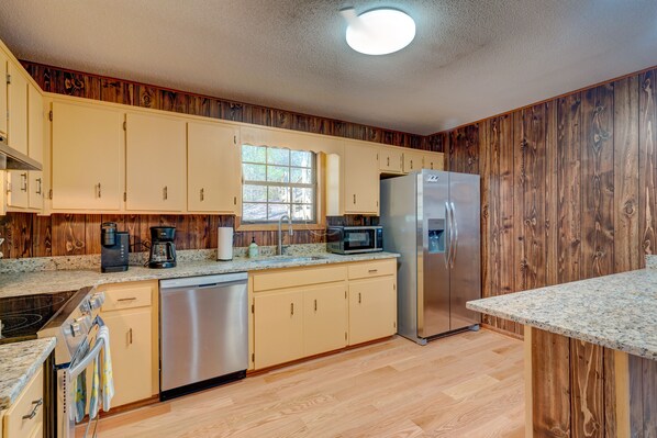 A kitchen with wooden paneling, a stainless steel refrigerator, a microwave, a coffee maker, and a dishwasher.