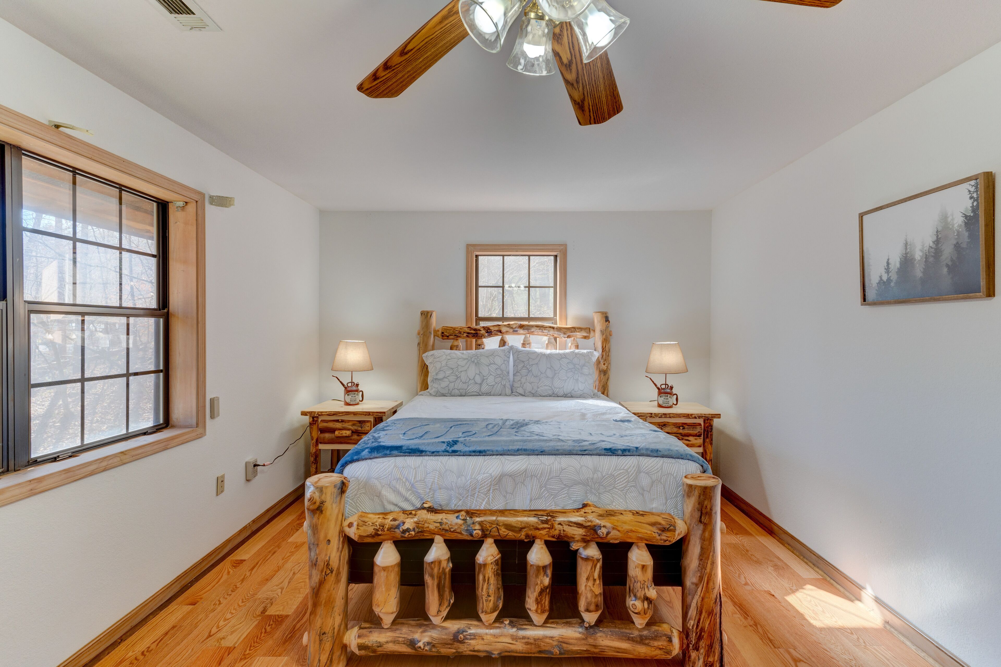 A bedroom with a wooden bed frame, a window, a ceiling fan, and a nightstand with a lamp.