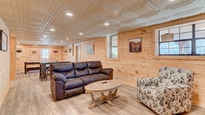 A log cabin interior with a brown leather sofa, floral-patterned armchair, and a round wooden table. - Wild Creek Cabin (Mineral Bluff)