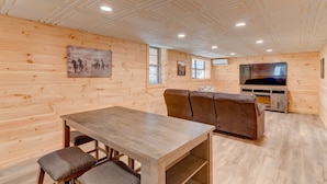 A wooden interior with a dining table, cushioned chairs, a sofa, and a television. - Wild Creek Cabin (Mineral Bluff)