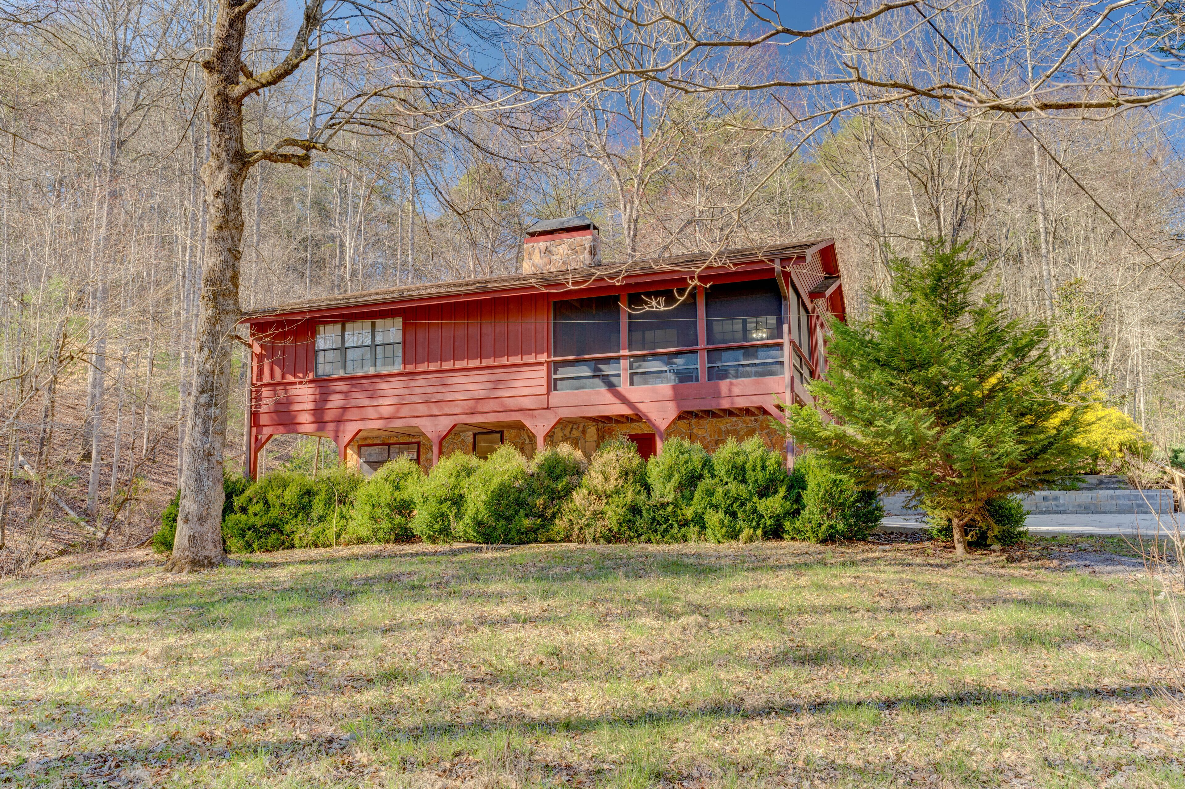 A red wooden cabin with a chimney, surrounded by trees and a grassy area.