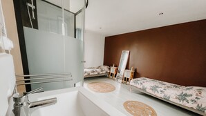 A modern bathroom with a large mirror, a white sink, and a bed with floral bedding. - cottage of the poste (Crouay)