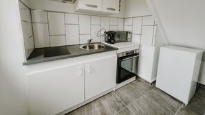 A compact kitchen with white cabinets, a stainless steel sink, a microwave, a coffee maker, and a built-in oven. - cottage of the poste (Crouay)