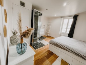 Ein Schlafzimmer mit Bett, Kleiderschrank, Badezimmer mit Glastür und einem Fenster mit Vorhängen.
