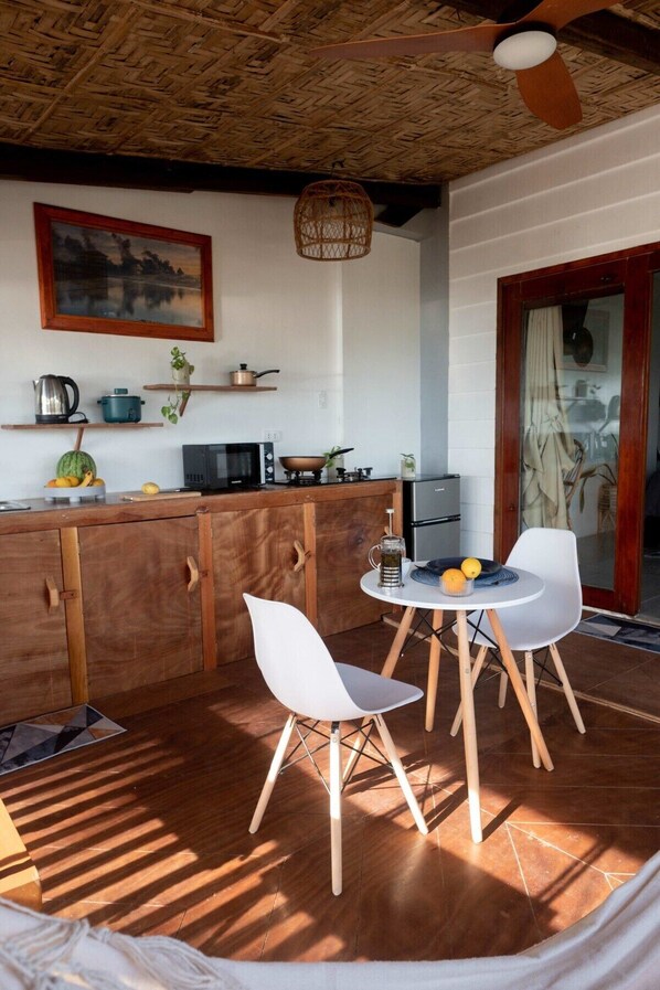A rustic kitchen with wooden cabinets, a dining table with chairs, a hanging light fixture, and a painting on the wall.