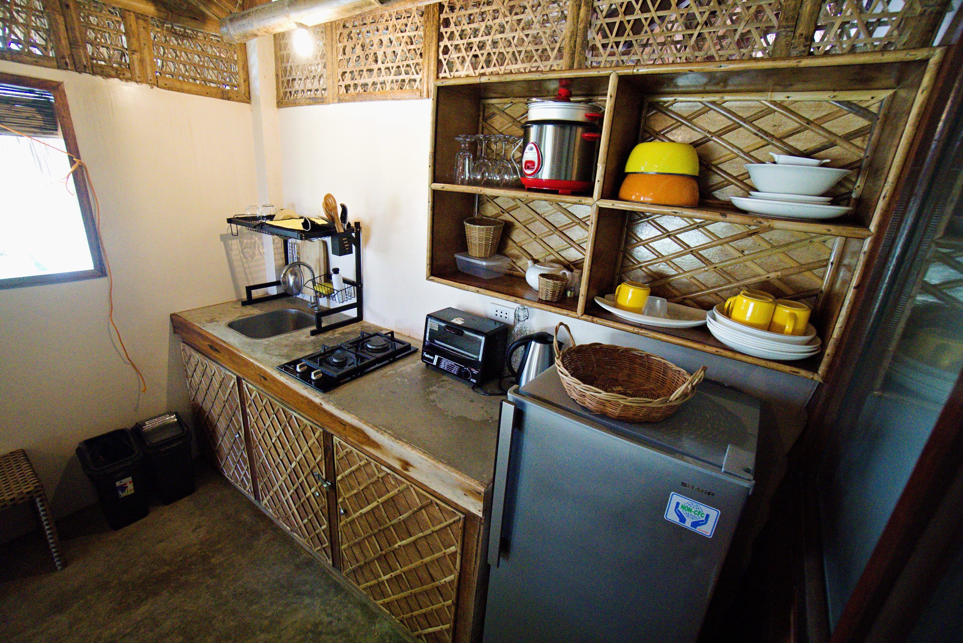 A compact kitchen with a gas stove, a toaster, a microwave, and a refrigerator. There are shelves with dishes and a basket on the counter.